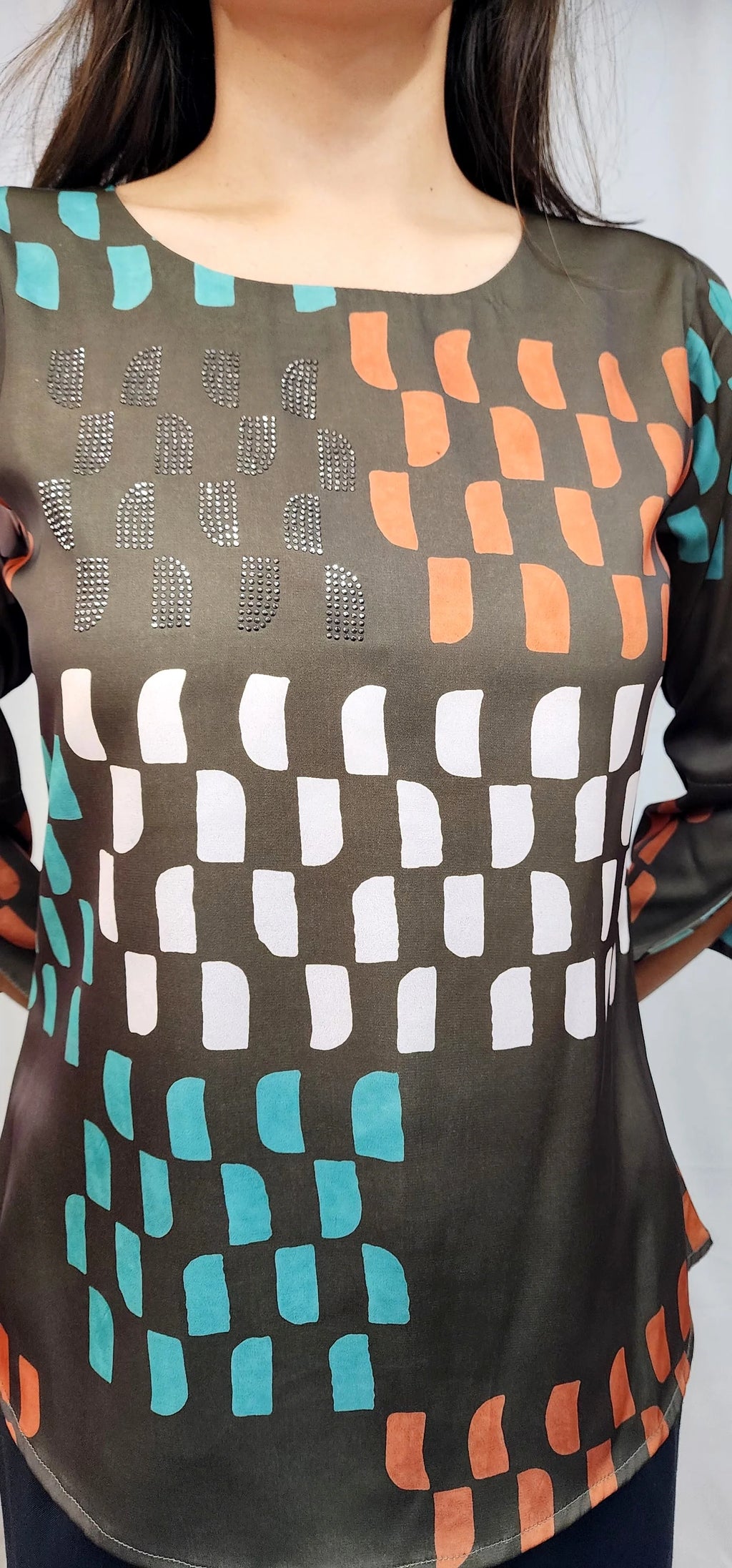 A close-up of a woman wearing a sheer black mesh top with a geometric pattern of white, orange, and teal shapes.