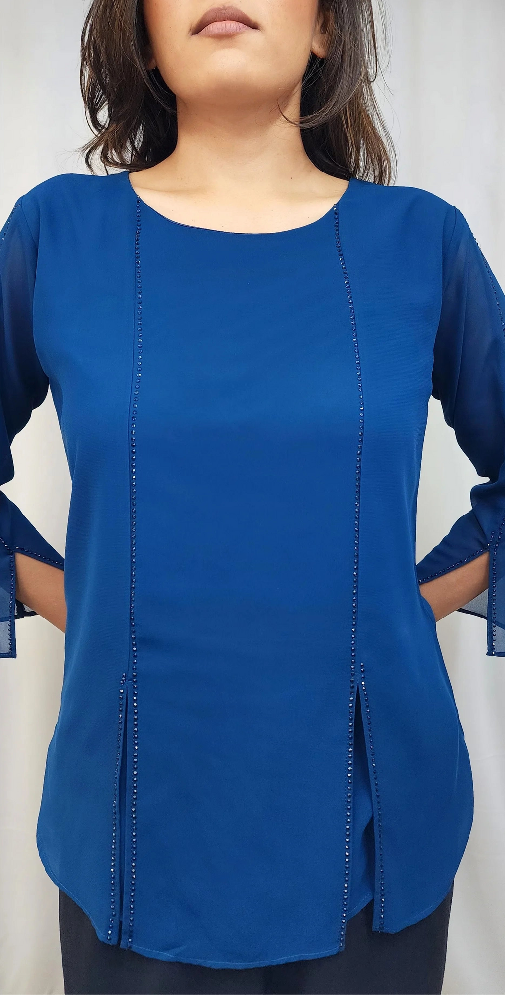A woman wearing a royal blue long-sleeve blouse with vertical decorative stitching down the front, shown against a light neutral background.