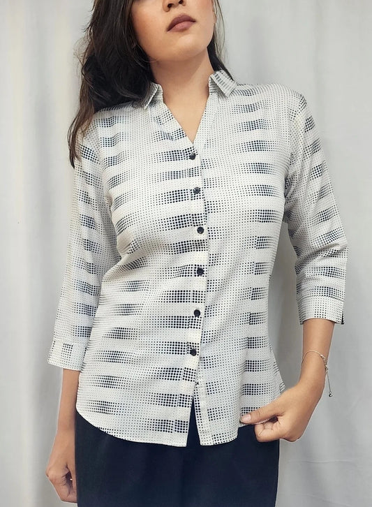 A woman modeling a light gray and white patterned button-up shirt with three-quarter sleeves, paired with dark navy pants, standing against a light gray curtain backdrop.