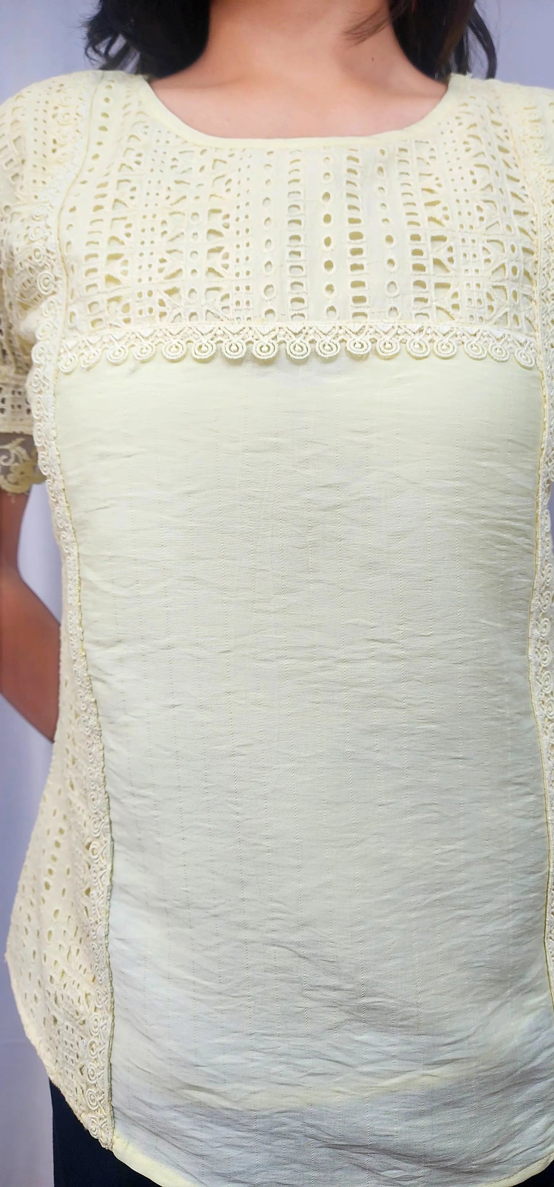 A pale yellow short-sleeve blouse with a textured, crinkled fabric body and a decorative crochet lace yoke with a scalloped edge.