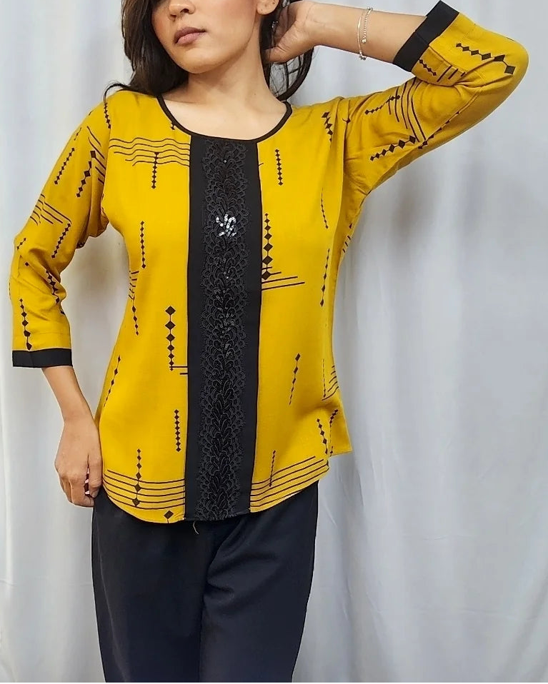A woman modeling a yellow and black printed kurta with three-quarter sleeves, standing in front of a white curtain inside what appears to be a clothing store.