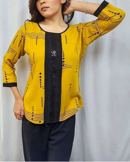 A woman modeling a yellow and black printed kurta with three-quarter sleeves, standing in front of a white curtain inside what appears to be a clothing store.
