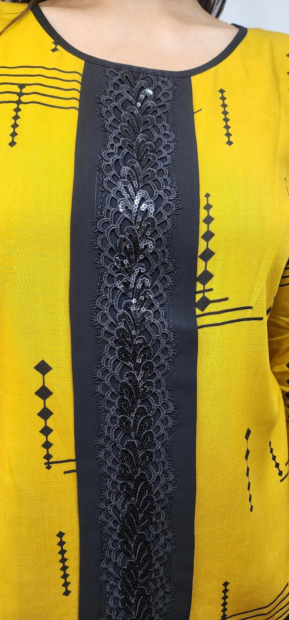 A close-up of a yellow kurta or tunic with a wide black central panel featuring intricate black embroidery and small sequins, plus black geometric line patterns on the yellow fabric.
