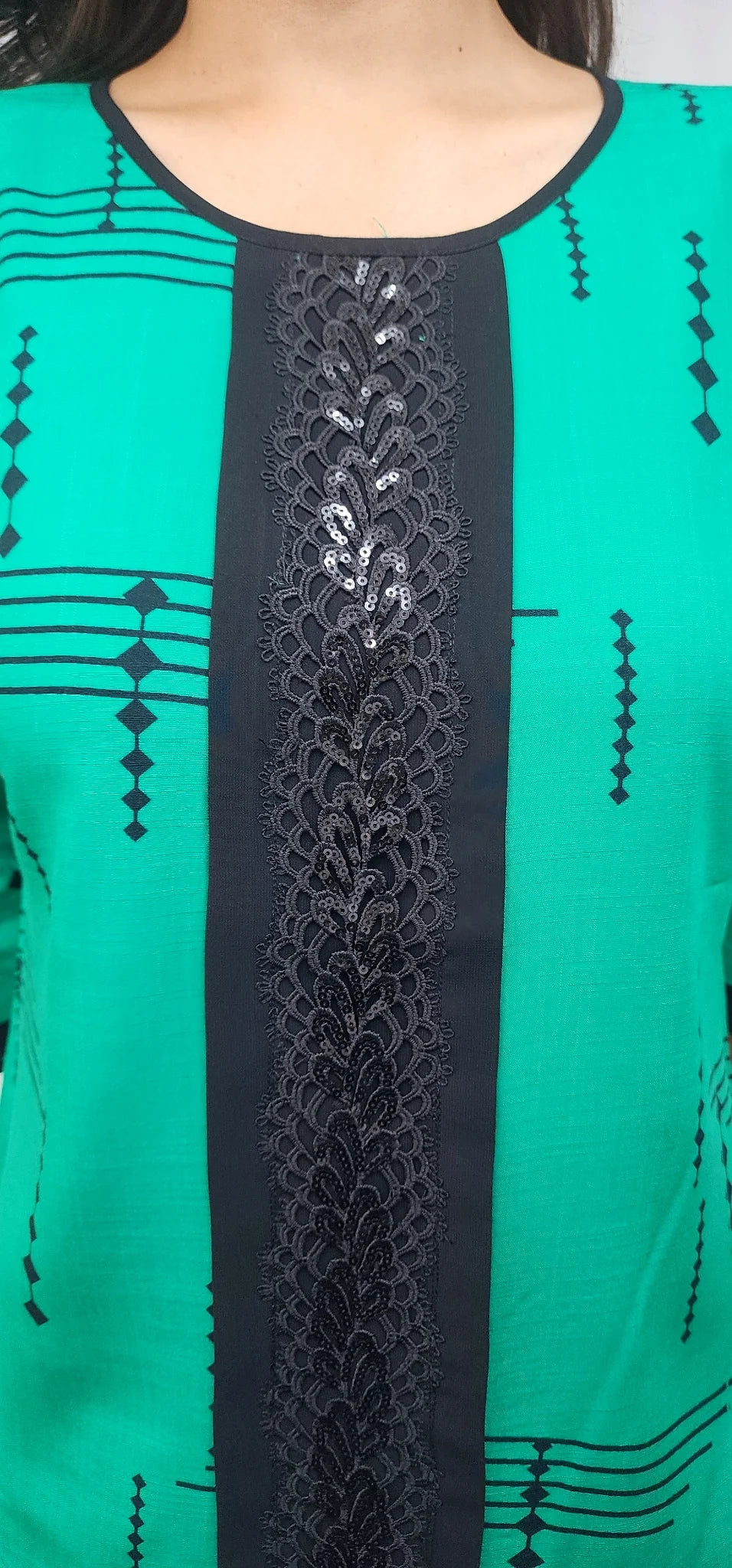 A close-up of a green kurta or tunic with a wide black central panel featuring black floral embroidery and sequins, along with black geometric patterns on the sides.