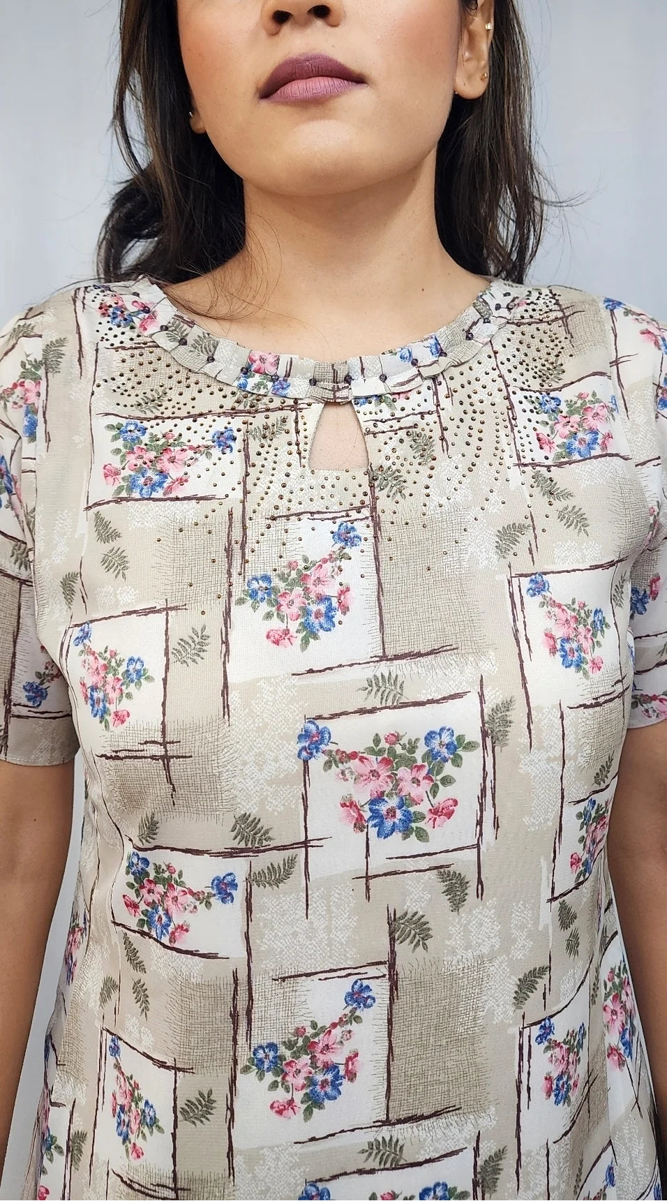 A woman wearing a beige short-sleeve kurta with a floral and geometric block print pattern, featuring a keyhole neckline with embroidered detailing.
