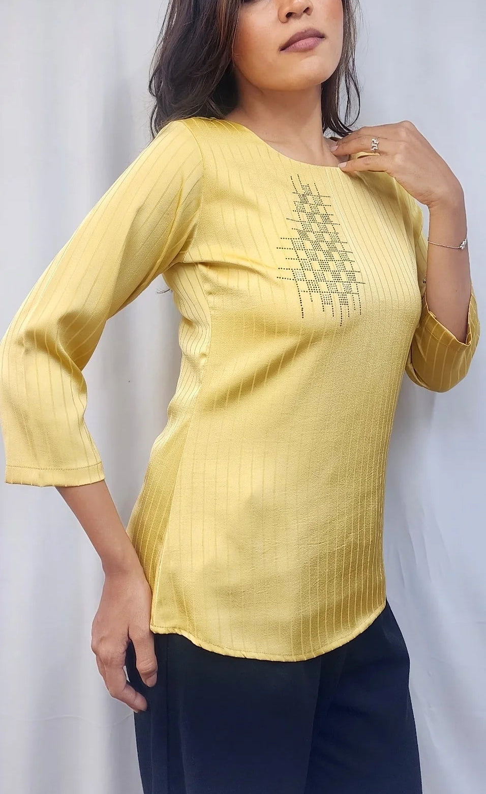A woman modeling a light yellow three-quarter sleeve kurta with a geometric embroidered pattern on the chest, paired with dark navy pants, set against a light gray draped fabric background.