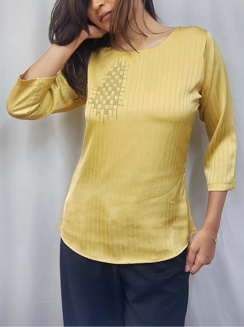 A woman wearing a yellow three-quarter sleeve kurta with a textured geometric pattern on the chest, paired with dark navy pants, posing in front of a white curtain.