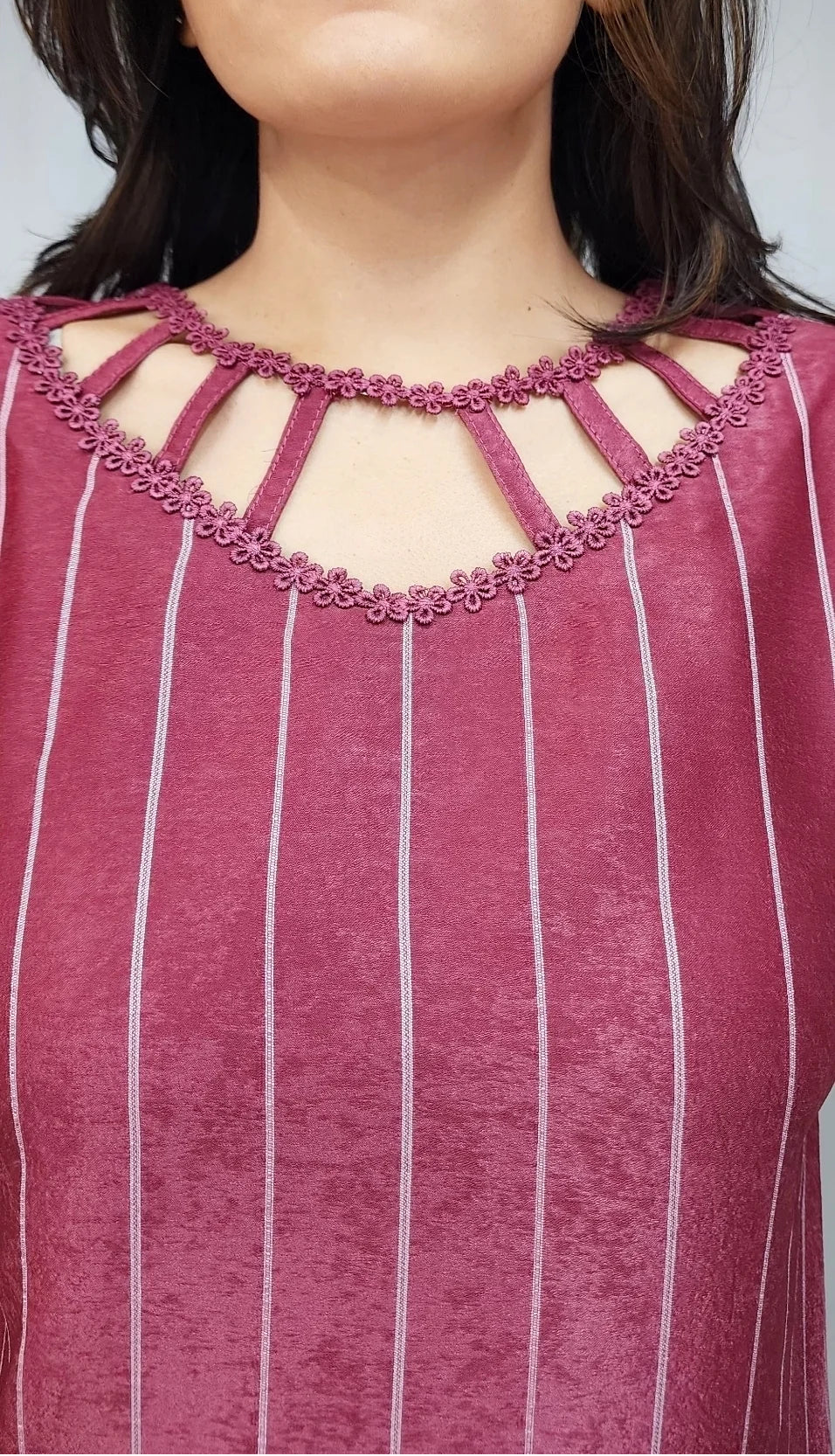 A close-up of a woman wearing a dusty rose pink top with vertical white stripes and a decorative cutout neckline with matching pink embroidery.