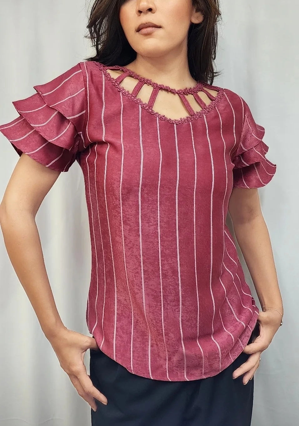 A woman modeling a dusty rose pink top with vertical white stripes, ruffled short sleeves, and a keyhole cutout at the neckline, paired with dark navy bottoms.